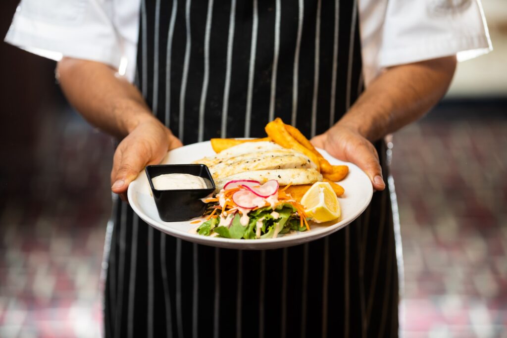 a chef holding a plate with a sandwich and chips
