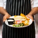 a chef holding a plate with a sandwich and chips